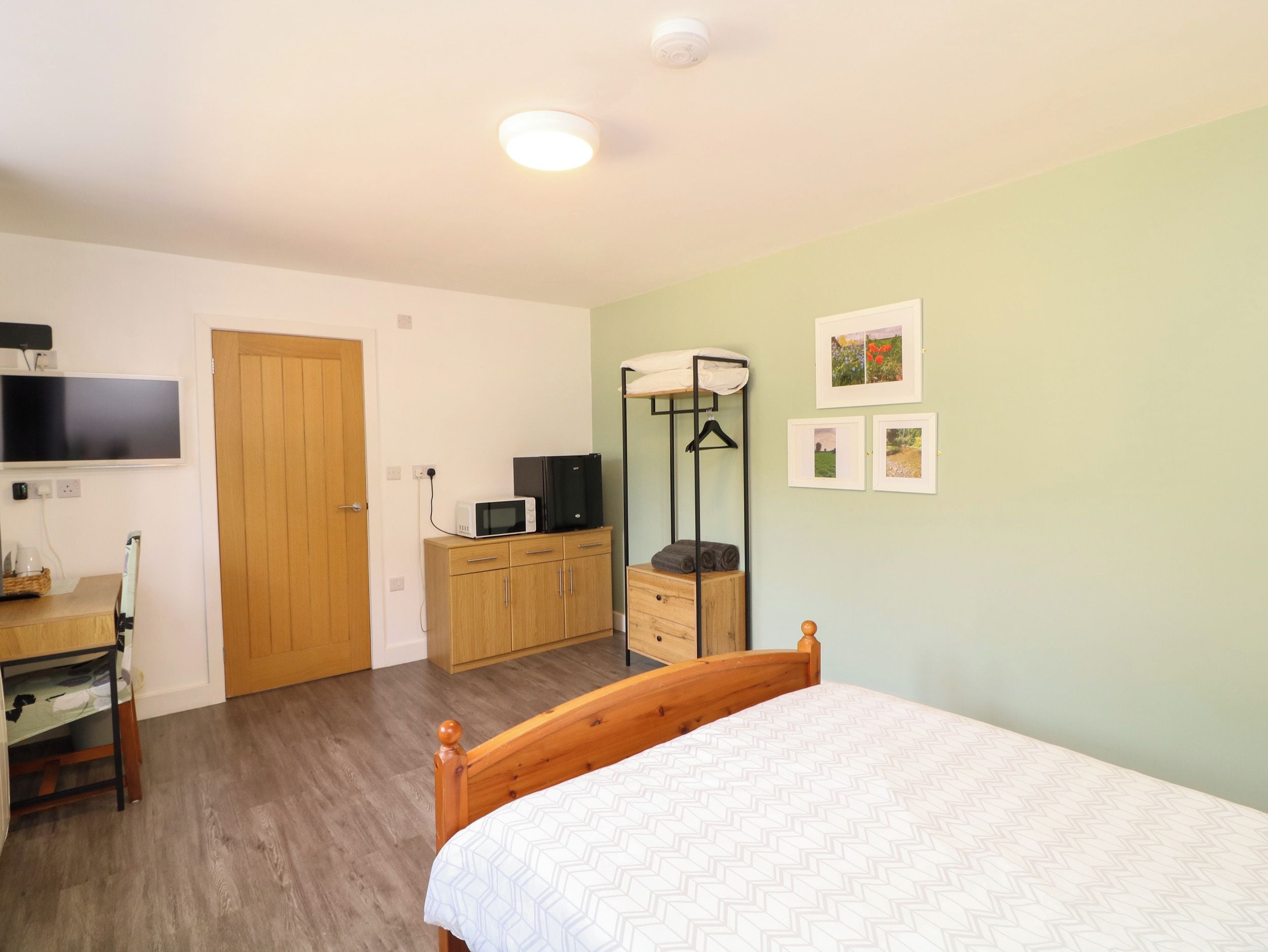 Ein Schlafzimmer mit einem hölzernen Bett, einem Kleiderschrank, einem Schreibtisch mit Flachbildfernseher und einer Mikrowelle auf einem Schrank.