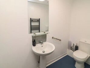 A bathroom with a white sink, a mirror, a towel rack, a toilet, and a blue floor.