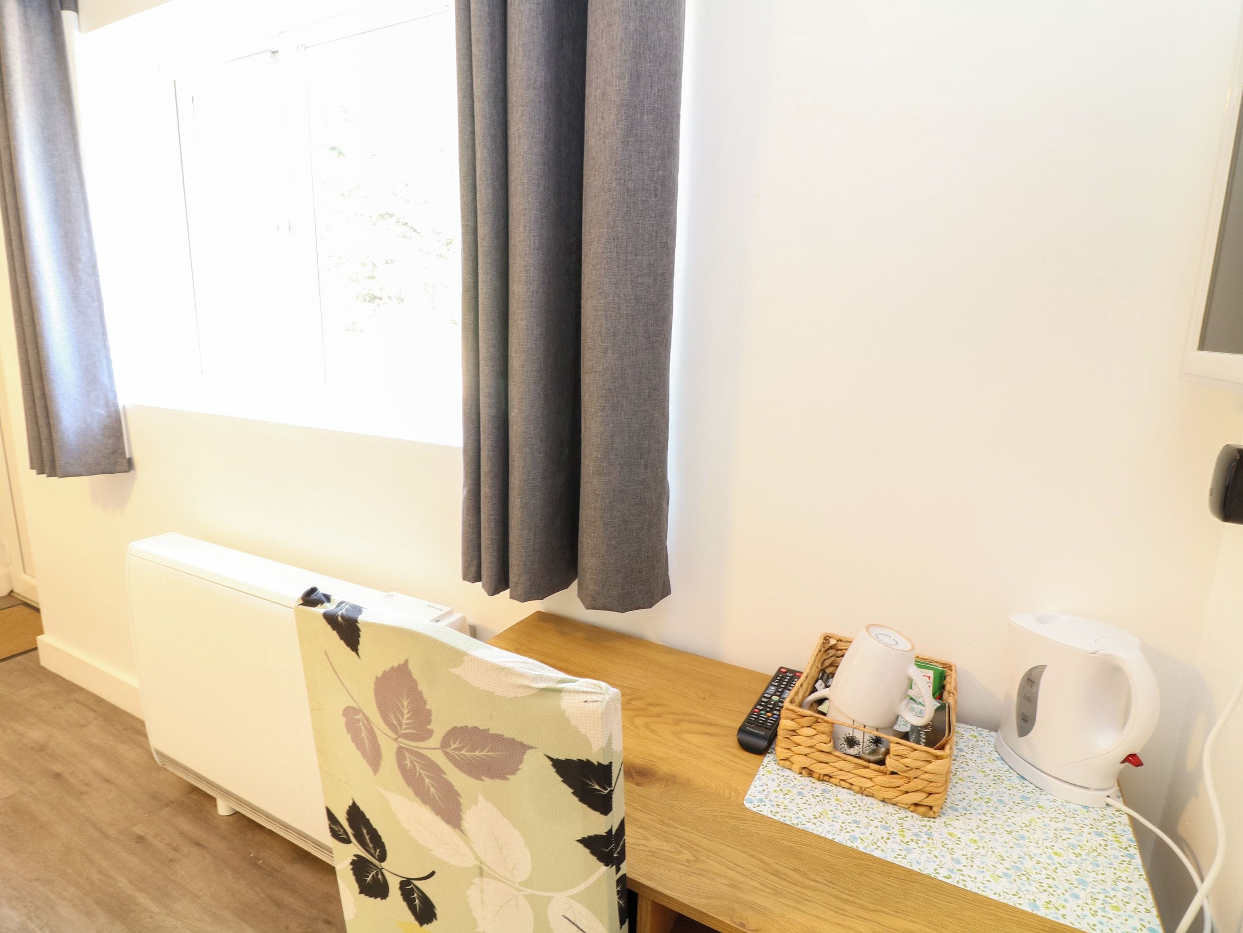 Une chambre avec un lit, une table en bois sur laquelle se trouve un panier contenant une bouilloire, une télécommande et une bouteille.