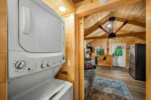 Une petite cabane en bois équipée d’une machine à laver, d’un réfrigérateur et d’un coin cuisine.