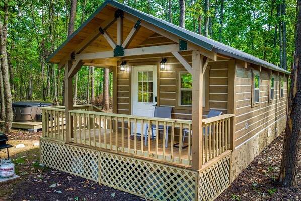 Une cabane en bois avec une véranda, un barbecue et une tente.