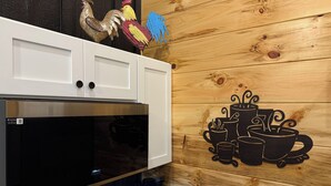 A kitchen with a large black microwave, white cabinets, and a wooden wall with a coffee-themed mural.