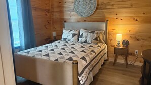 A wooden-paneled room with a bed, a round wall decoration, a bedside lamp, and a small table.