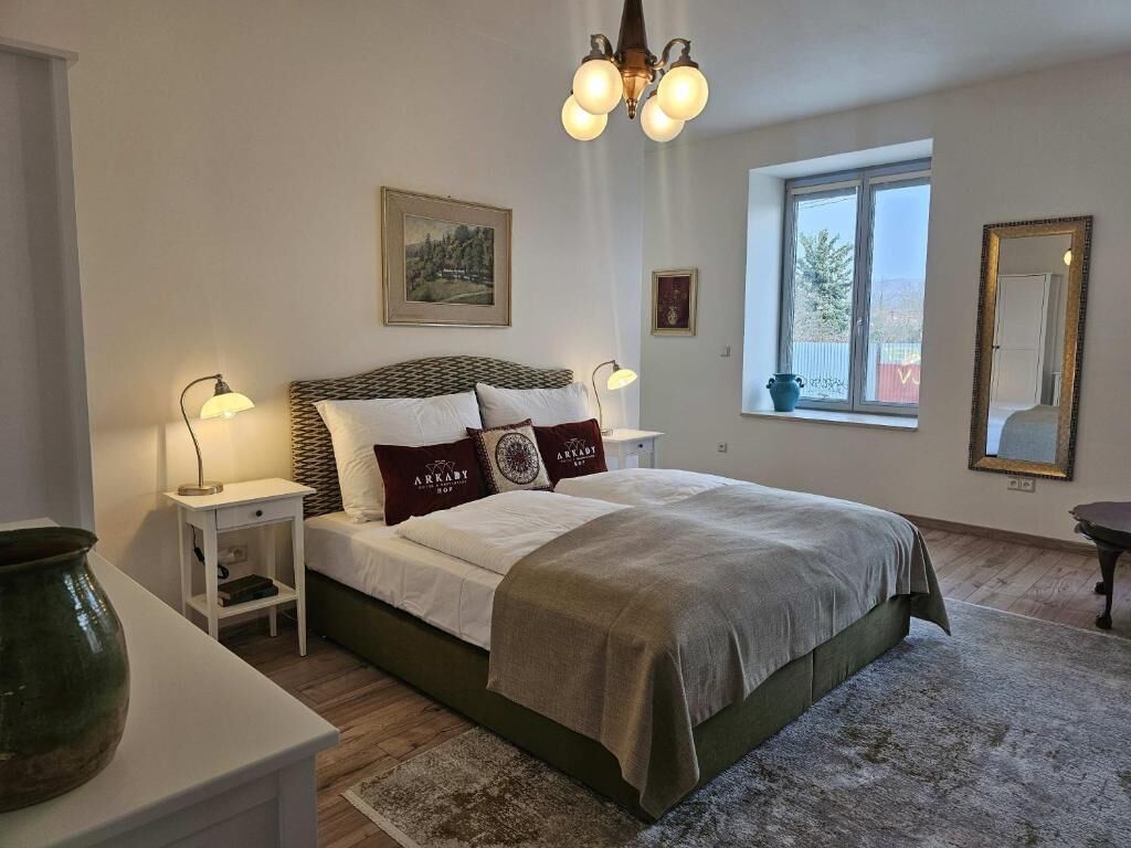 A bedroom with a bed, bedside tables, a lamp, a window, and a mirror.