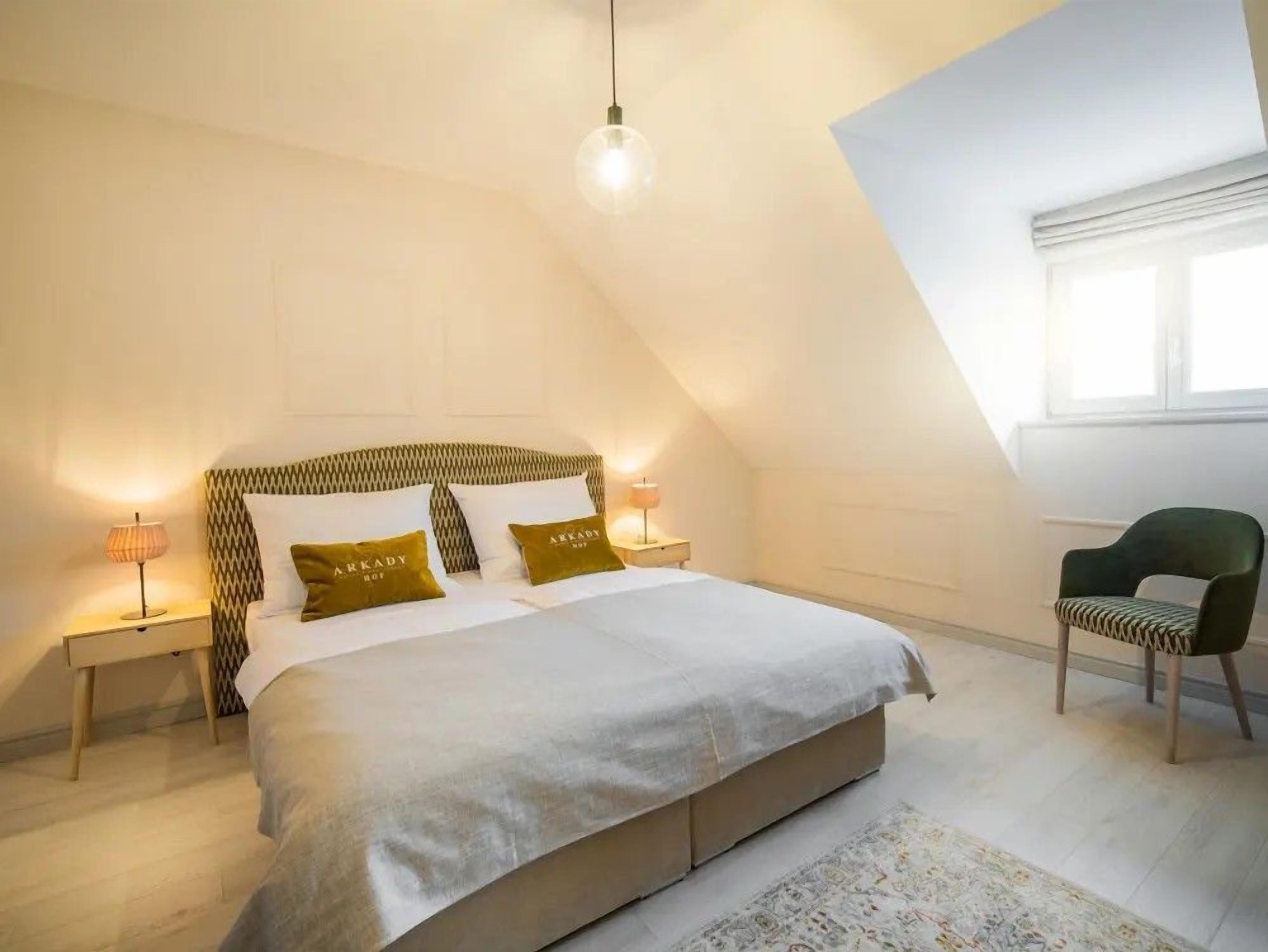 A bedroom with a bed, bedside lamps, a chair, and a window.