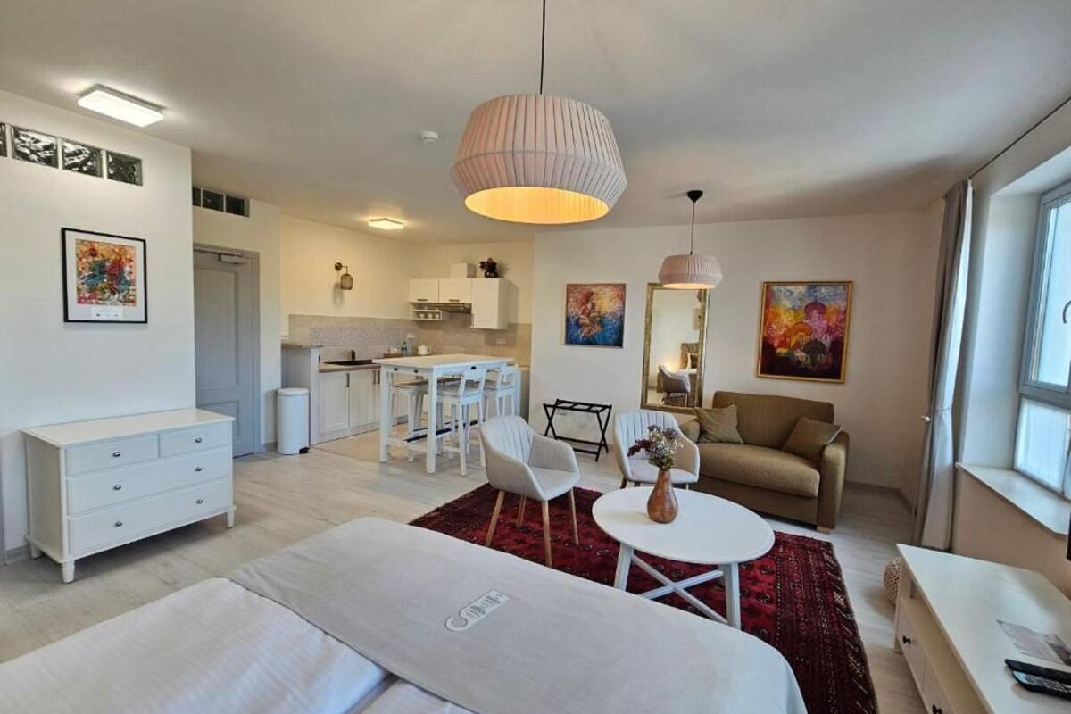 Una habitación de hotel moderna con cama, zona de comedor, sofá y cocina al fondo.