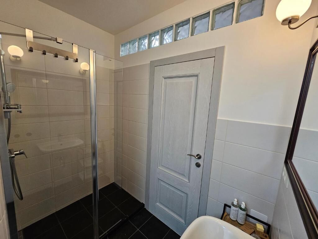 A bathroom with a glass shower enclosure, a white door, and a sink with toiletries.