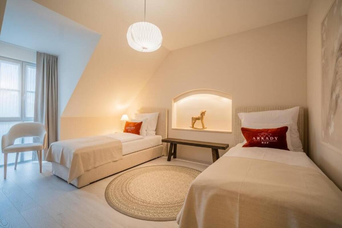 Habitación de hotel con dos camas, un tapete redondo, un banco y una lámpara fijada a la pared.