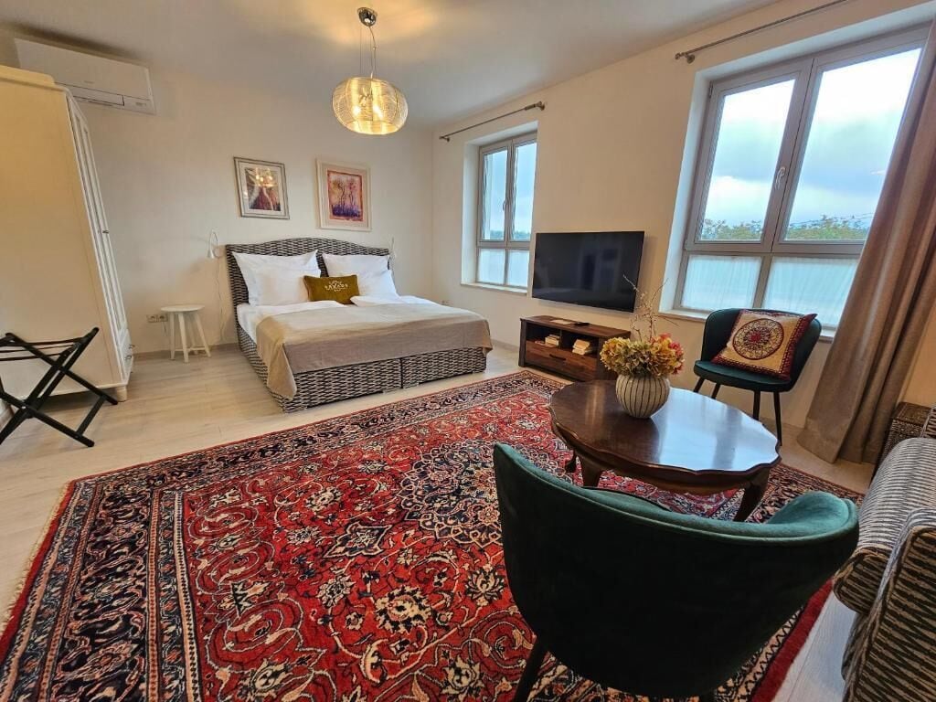 A bedroom with a bed, a TV, a large window, and a view of the sky.
