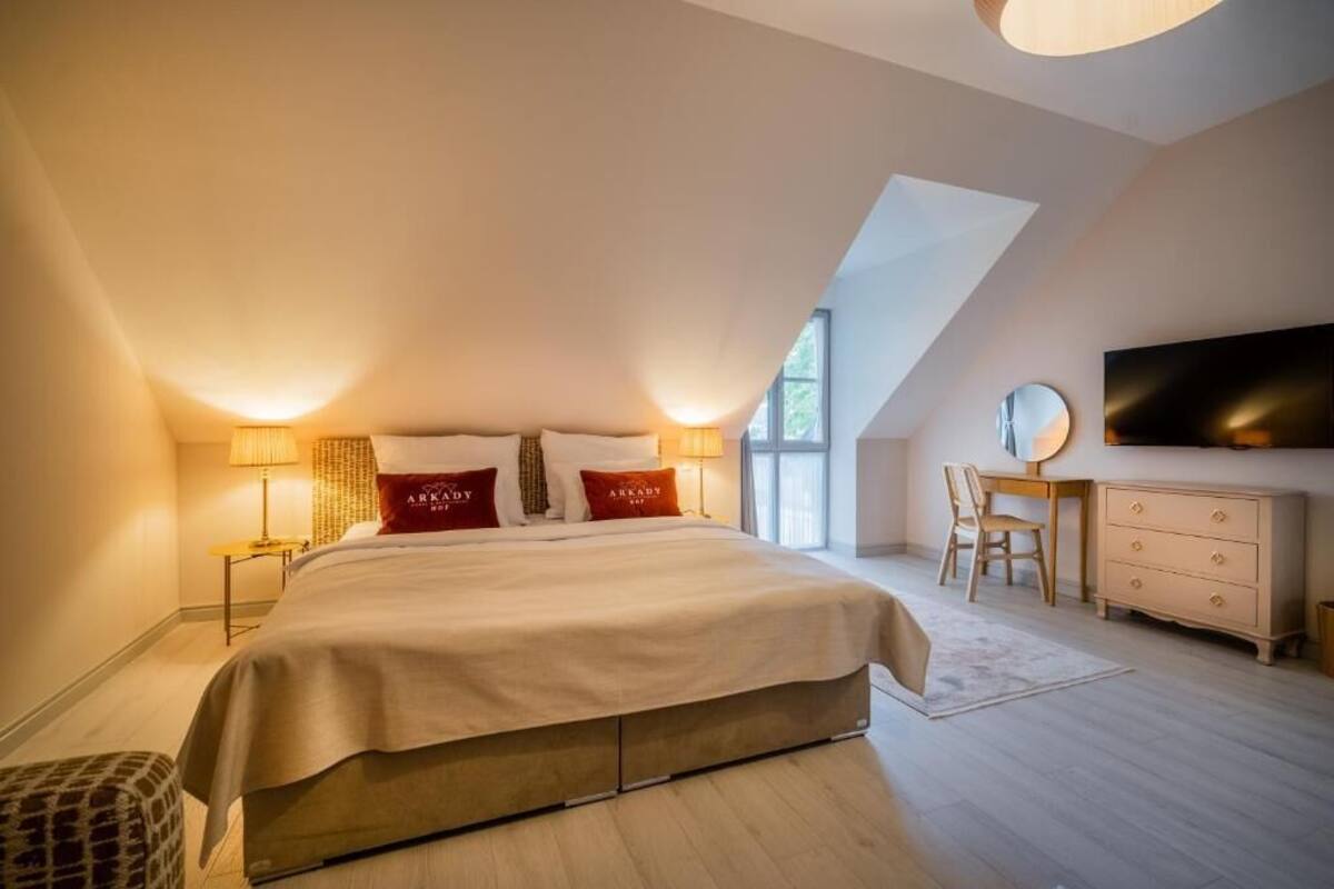 Un dormitorio con una cama grande, dos lámparas de noche, un escritorio con una silla, un aparador y un televisor montado en la pared.