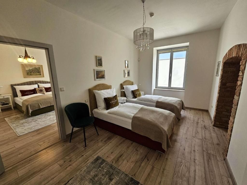 A bedroom with two beds, a chair, a chandelier, and a stone archway.
