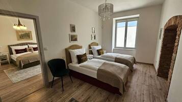 A bedroom with two beds, a chair, a chandelier, and a stone archway.