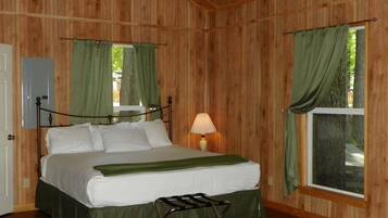 A wooden-paneled room with a bed, a nightstand, a lamp, and a window with curtains.
