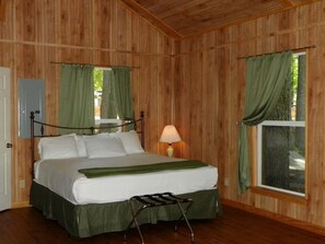 Una habitación con paneles de madera, una cama, una mesita de noche, una lámpara y una ventana con cortinas.