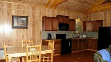 A wooden-paneled kitchen with a dining table and chairs, a microwave, a stove, and a refrigerator.