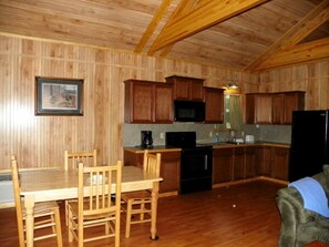 Cocina con paneles de madera, mesa y sillas, microondas, estufa y refrigerador.