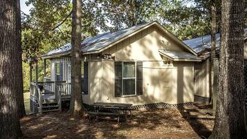 A small, single-story cabin with a porch, surrounded by trees.