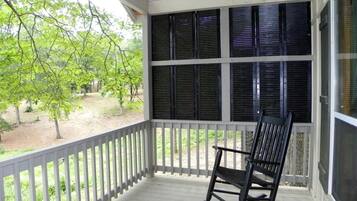 A porch with a rocking chair, white railing, and large windows with shutters.