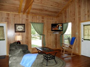 Una habitación con paredes de madera, un sofá, una mesa, un sillón mecedora y un televisor.