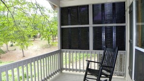Une véranda avec un fauteuil à bascule, une balustrade blanche et de grandes fenêtres dotées de volets.
