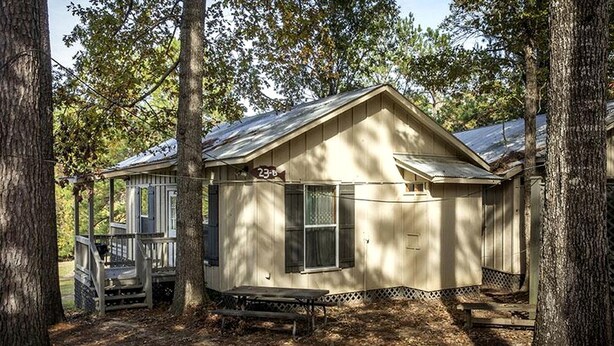 Une petite cabane à un seul étage, dotée d’un porche et entourée d’arbres.
