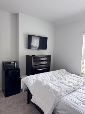 Une chambre à coucher comprenant un lit, une commode, un téléviseur et un four à micro-ondes.