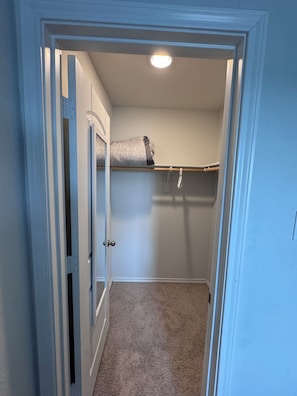 Un petit placard fermé avec une porte, un luminaire au plafond et un lit recouvert d’une couverture à motifs.