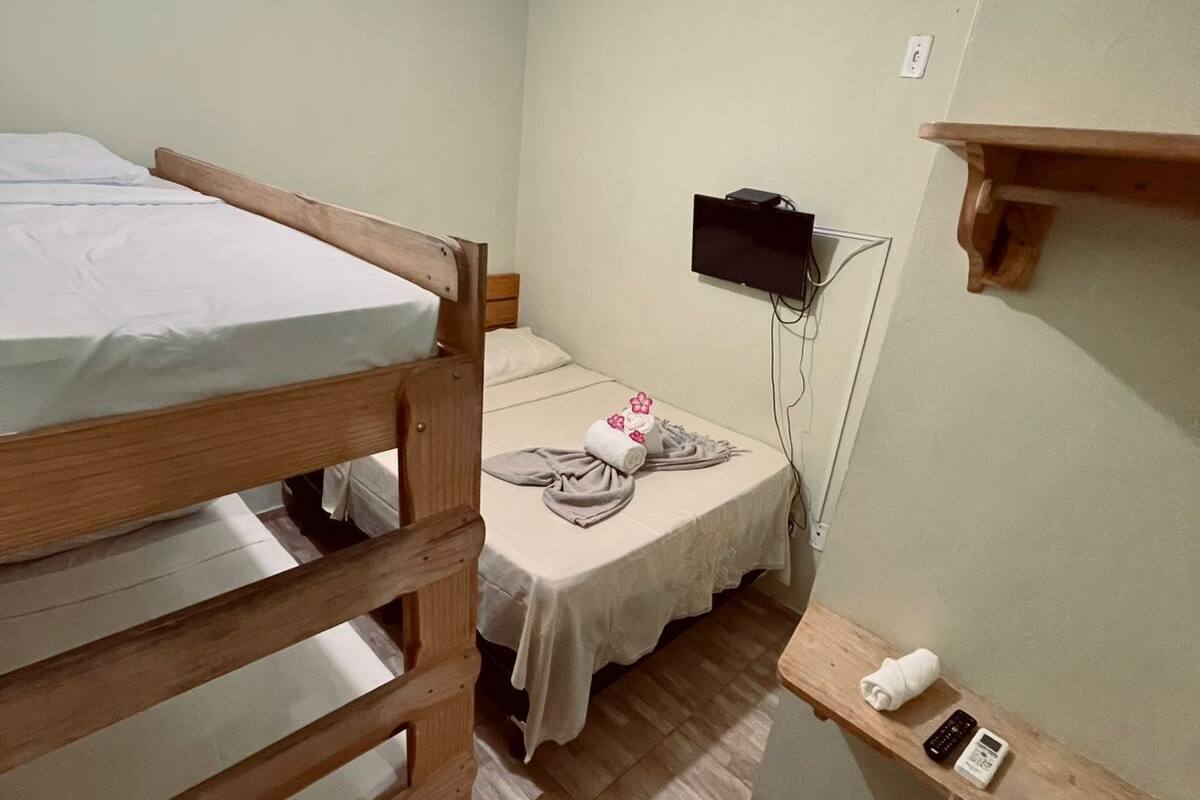 Una habitación con una cama litera, una cama individual, un televisor montado en la pared, un estante pequeño con un teléfono y un control remoto, y un refrigerador.