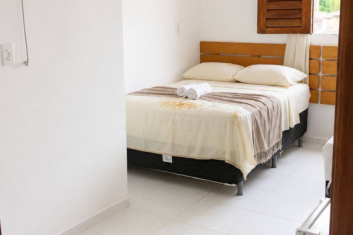 Un dormitorio con cama, ventana con contraventanas de madera, ventilador de techo y aire acondicionado instalado en la pared.