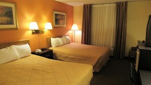 Habitación de hotel con dos camas, un escritorio, una silla, un televisor y dos lámparas de pared.