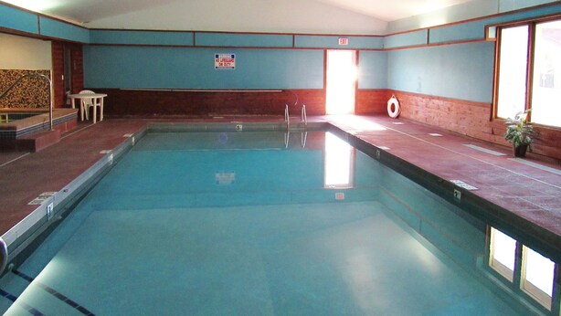 Una piscina interior con un cartel de salvavidas, una pequeña mesa y una planta en maceta.