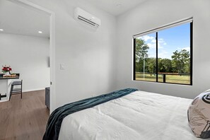 A bedroom with a bed, a window with a view of a park, and a small desk with a chair.