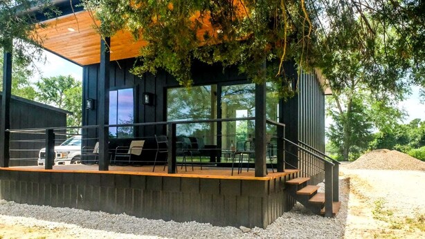 Ein modernes Gebäude mit einer Holzterrasse, Sitzgelegenheiten im Freien und großen Fenstern.