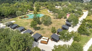 An aerial view of a resort with multiple cabins, a swimming pool, and surrounding greenery. - Family-Friendly Tiny Home Resort with Pool, Goats & Pond in Hempstead near Houston (Hempstead)