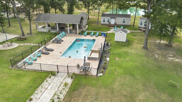 A swimming pool with lounge chairs, a covered patio, and a small shed.