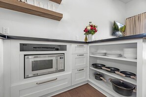 Une cuisine moderne avec des meubles blancs, un four à micro-ondes encastré, une étagère contenant des ustensiles de cuisine et un vase avec des fleurs.
