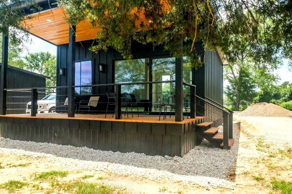 A modern building with a wooden deck, outdoor seating, and large windows. - Family-Friendly Tiny Home Resort with Pool, Goats & Pond in Hempstead near Houston (Hempstead)