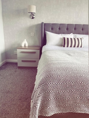 A bedroom with a bed, a nightstand, a lamp, and a wall outlet.