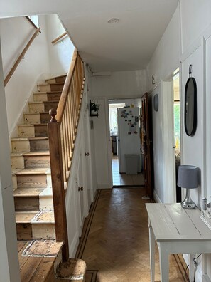 Eine Treppe führt zu einer Zwischenebene, eine weiße Tür, ein Kühlschrank und ein Tisch mit einer Lampe.