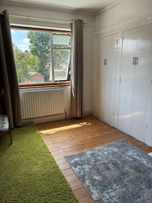 Une pièce avec une fenêtre, un radiateur, un plancher en bois, un tapis vert et une armoire.