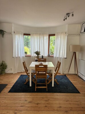 Ein Essbereich mit Tisch, Stühlen, einer Lampe und Blick auf Grünanlagen durch Fenster.
