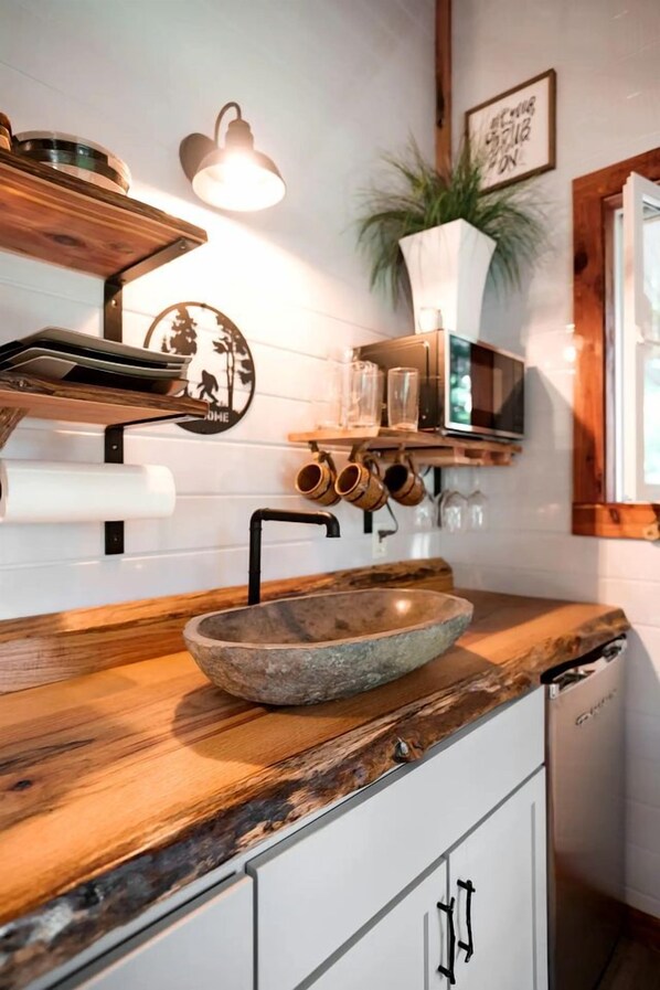 Eine Küche mit Spüle aus Stein, Holz Arbeitsplatte, hängenden Tassen und einem Topf mit Pflanze.