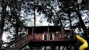 A wooden deck with a yellow slide, surrounded by trees.