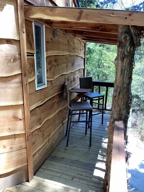 A wooden cabin with a deck, a window, and a table with chairs. - Enchanting Forest Treehouse Hideaway with Farm Activities near Bingham Creek in Forestburg, Texas (Forestburg)