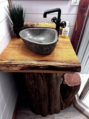 Une salle de bain rustique avec un lavabo en pierre, un plan de toilette en bois et un robinet noir.