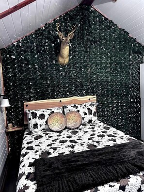 Un dormitorio con cama, cabecera de madera, decoración de cabeza de venado y pared cubierta de hojas verdes.