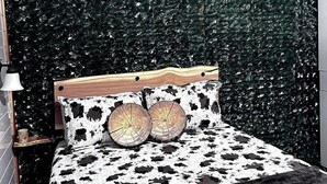 A bedroom with a bed, a wooden headboard, a deer head decoration, and a green leafy wall.