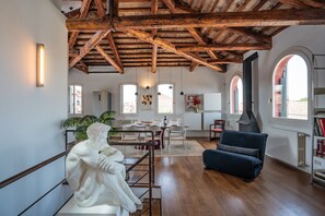 Ein geräumiger Raum mit hoher Holzbalkendecke, einer Essecke mit Tisch und Stühlen, einer Couch, einem Kamin und großen Fenstern.