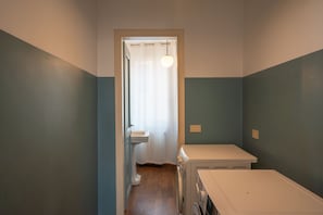 Ein kleines, schmales Badezimmer mit Toilette, Waschmaschine und einer Lampe.