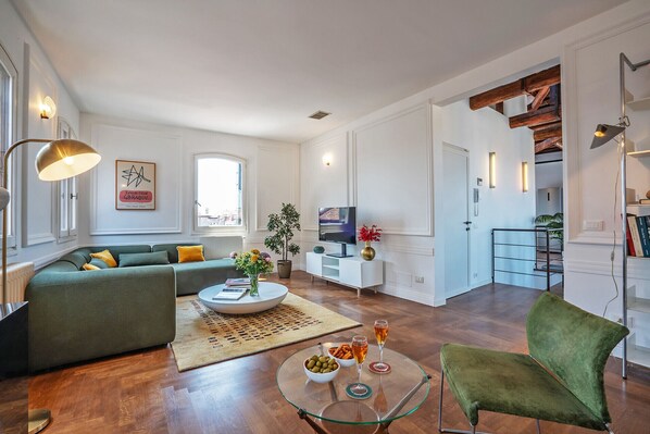 A modern living room with a sofa, a glass coffee table, a TV, and a staircase. - Corte delle Candele Rooftop Views (Venice)
